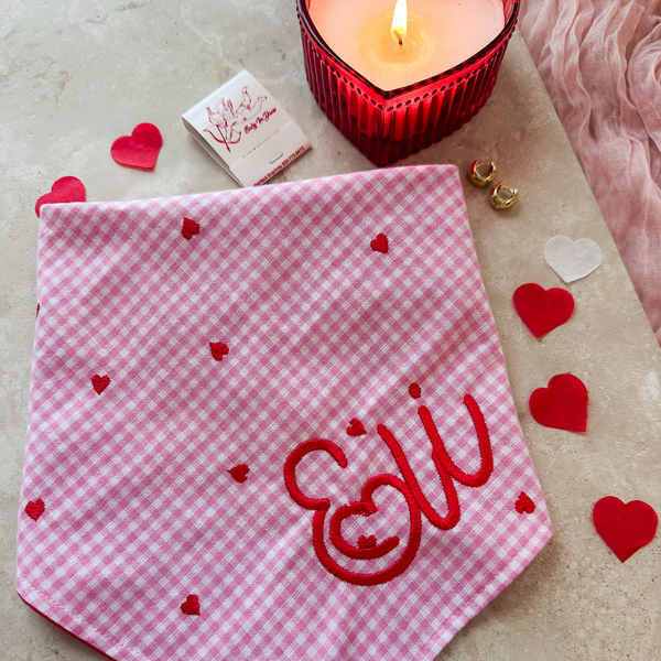Pink checkered towel with red hearts and 'Elly' embroidery, surrounded by heart-shaped decorations and a lit candle.